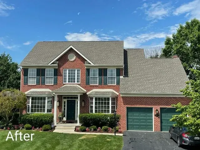 Large 2-story brick home with a new gray shingle roof, white gutters, and green garage door with grassy front lawn and trees surrounding