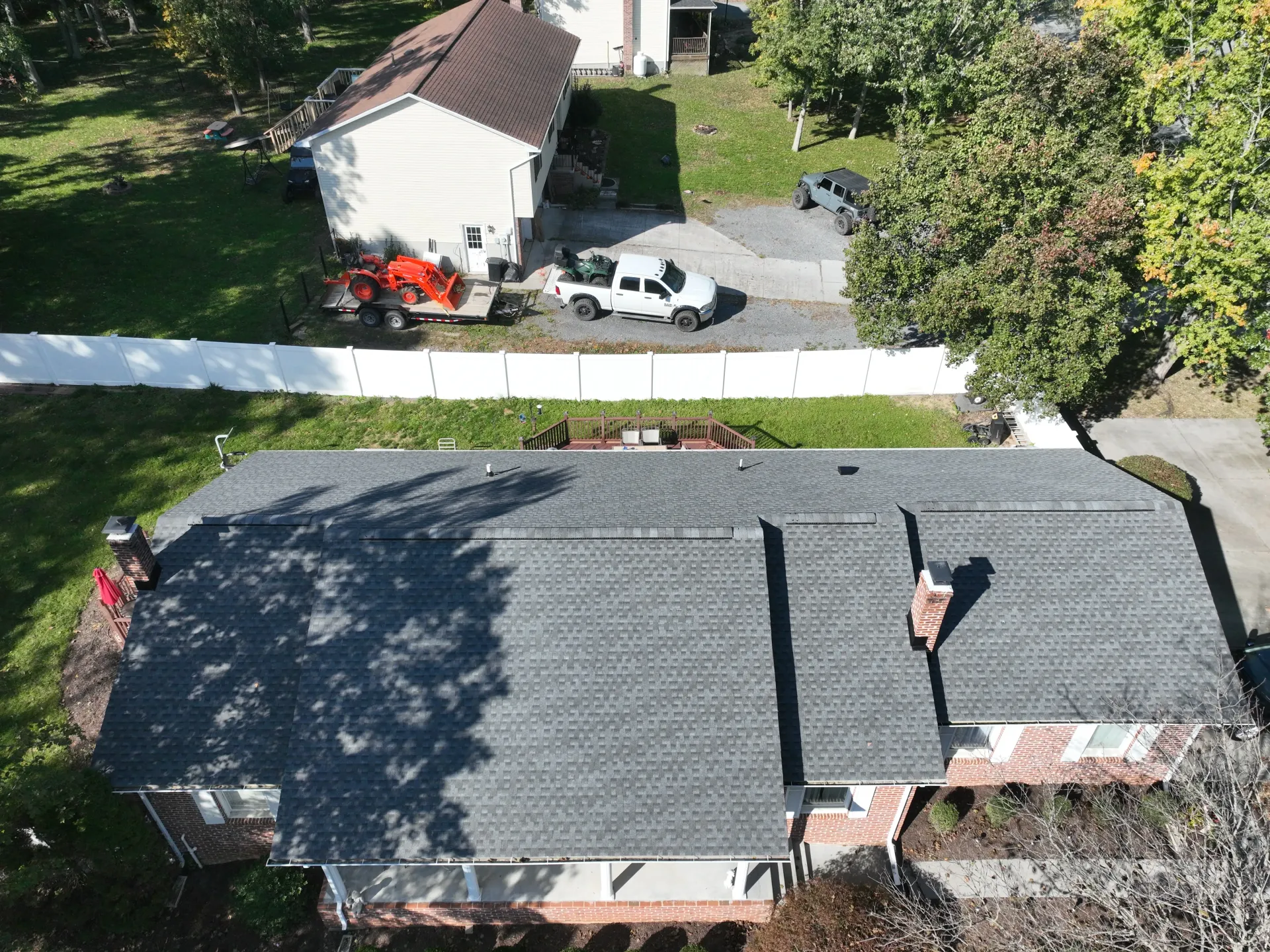 Aerial view of a red brick home with a new dark gray shingle roof, surrounded by trees