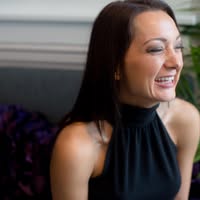 Profile picture of a smiling brunette woman wearing a black dress