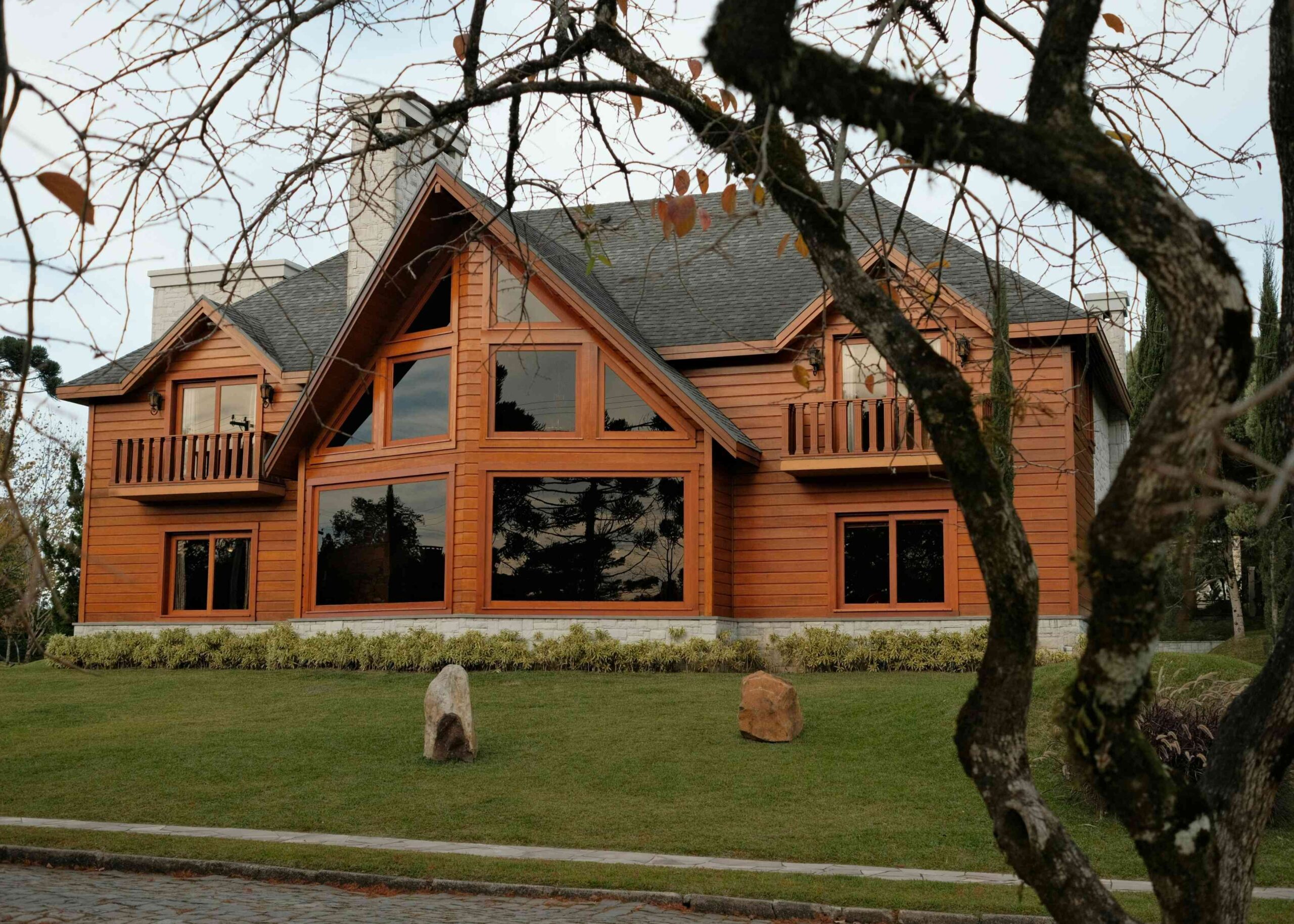 Street view of a large A-frame window wooden home with many windows and a large pitched roof with dark gray shingles