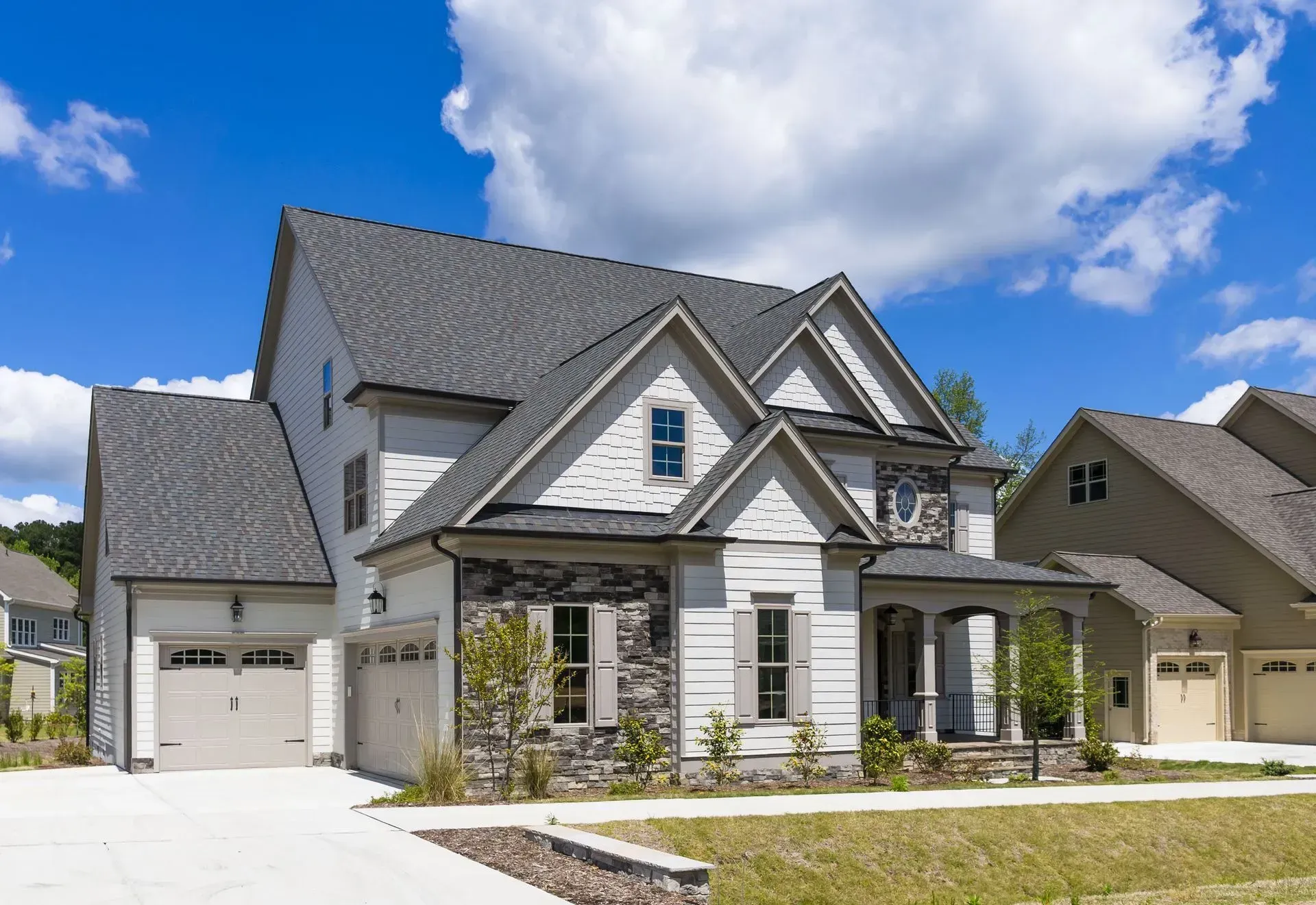 A large 2-story home with natural stone, white siding, and a gray roof with a sunny sky above