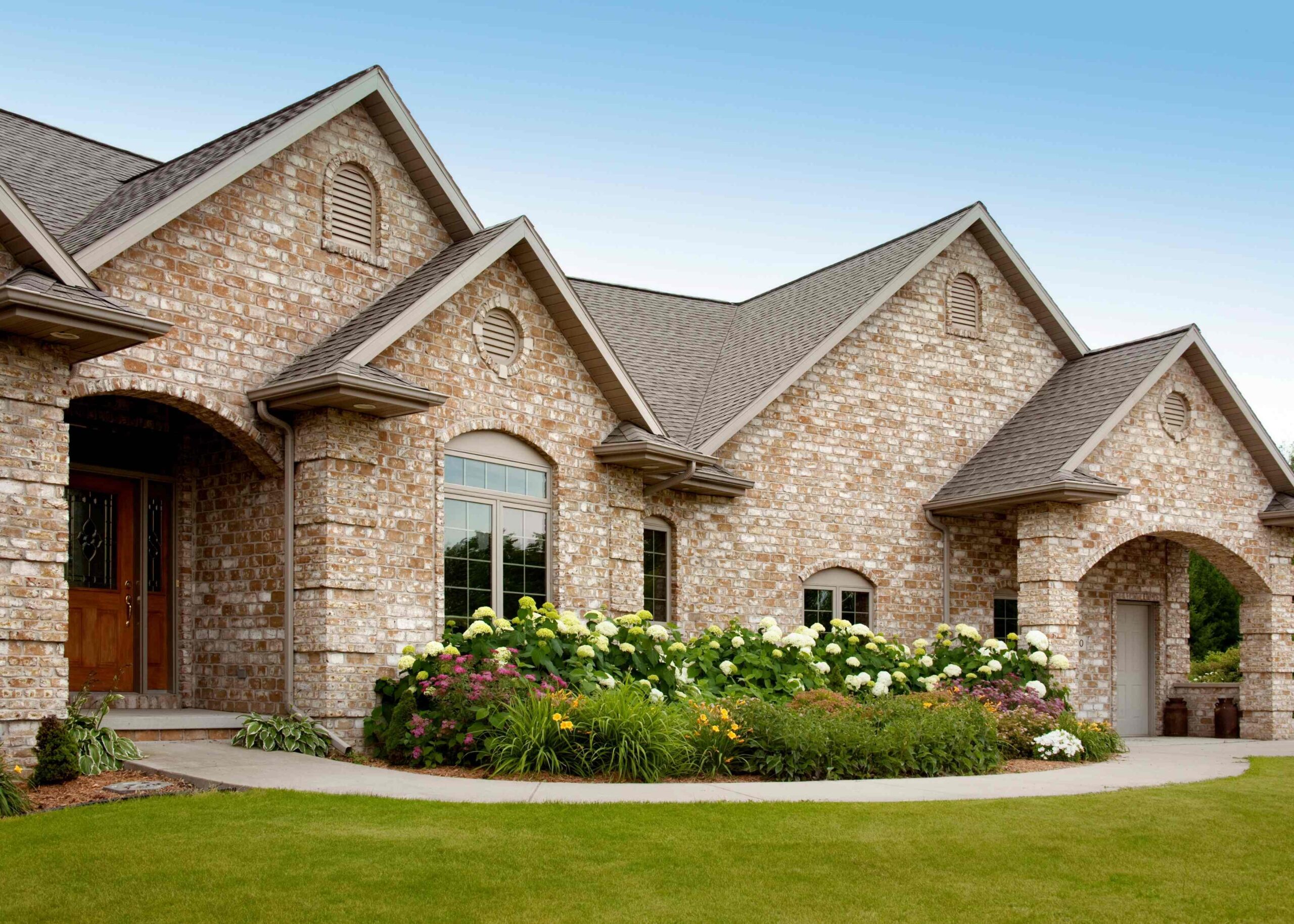 A large, sturdy stone house with a sloped roof and surrounded by greenery