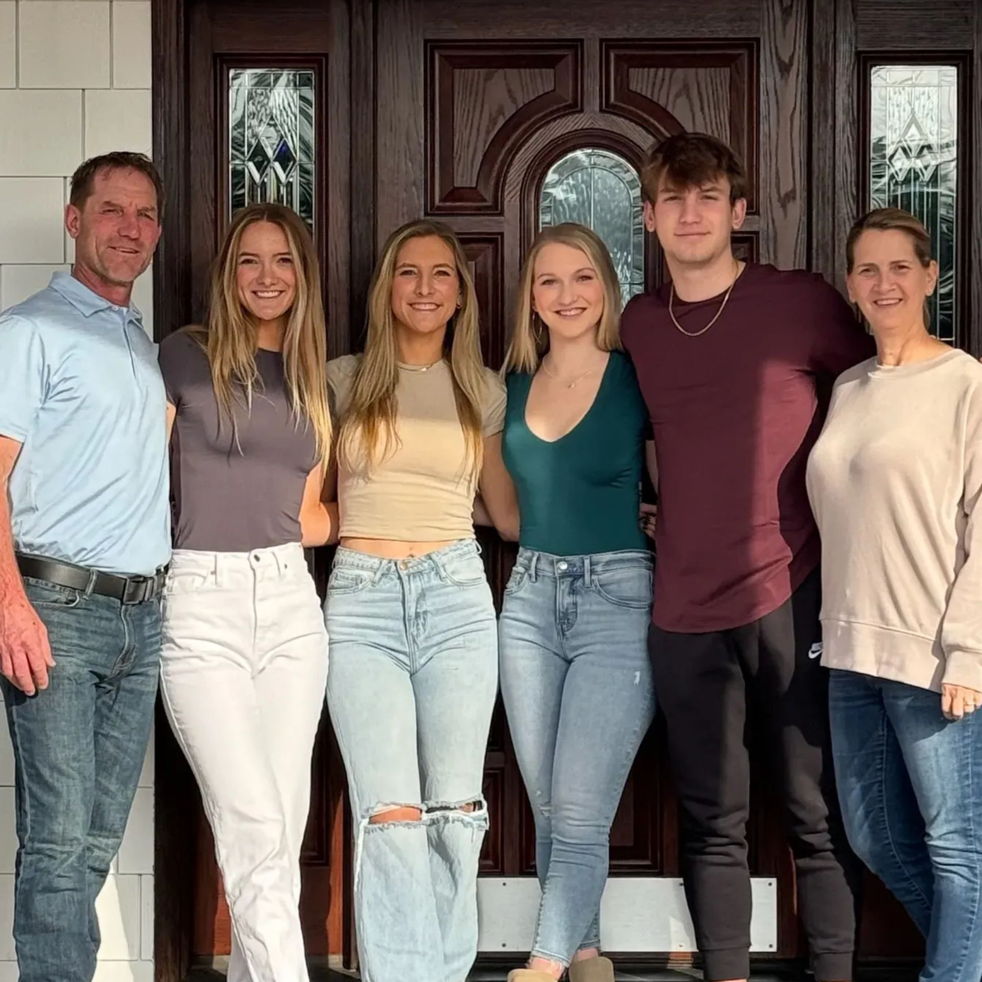 A smiling family of 6, including (from left to right), a father, 3 daughters, a son, and a mother