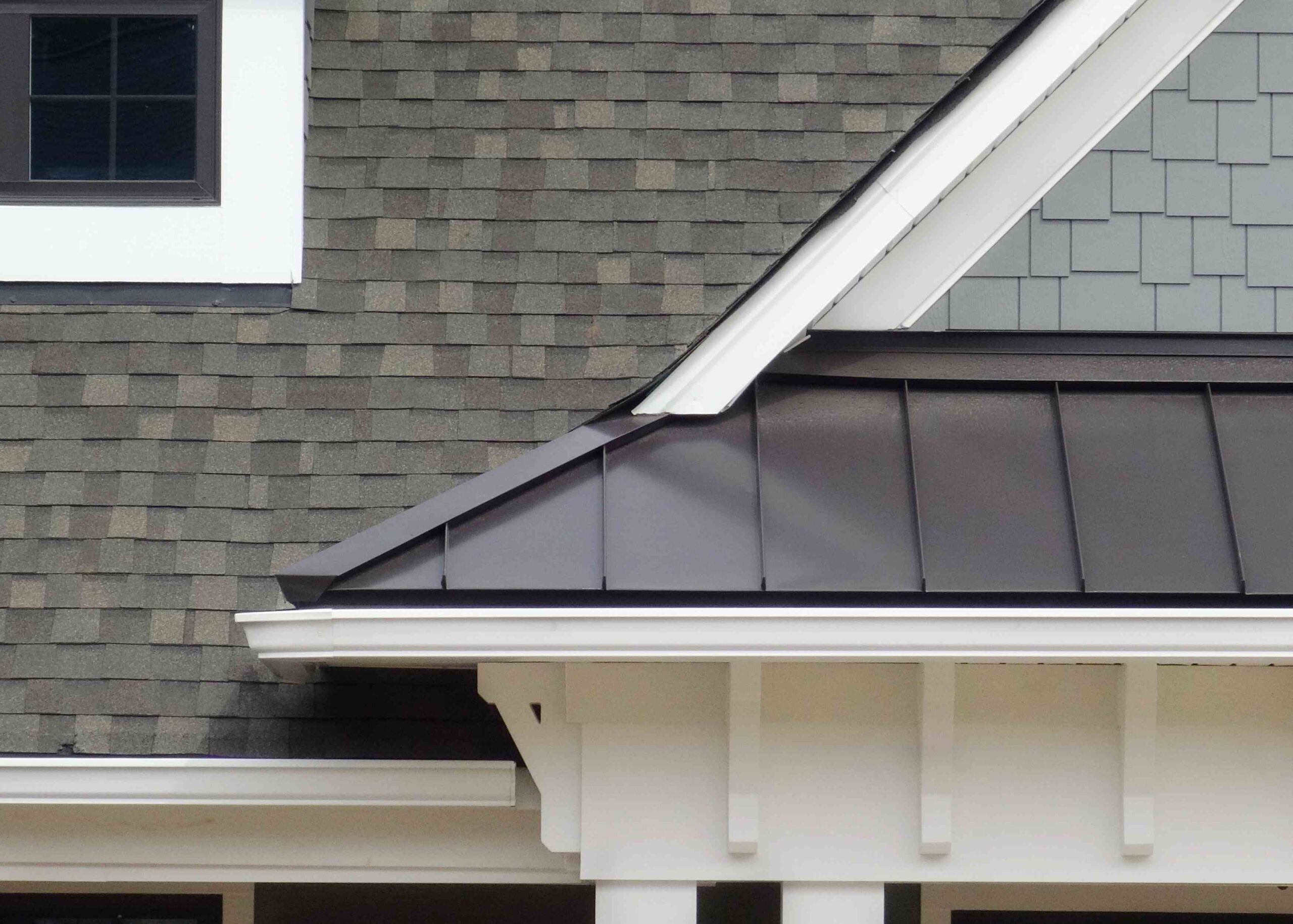 Close up view of a home with white gutters, mixed gray shingles, and black metal roofing