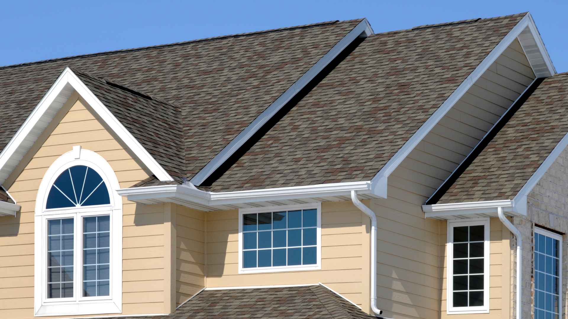 Yellow house exterior featuring a multi-pitched roof with grey asphalt shingles, white trim, and various windows