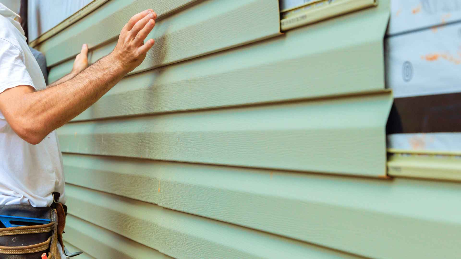 Closeup of a man installing light green vinyl siding on a house